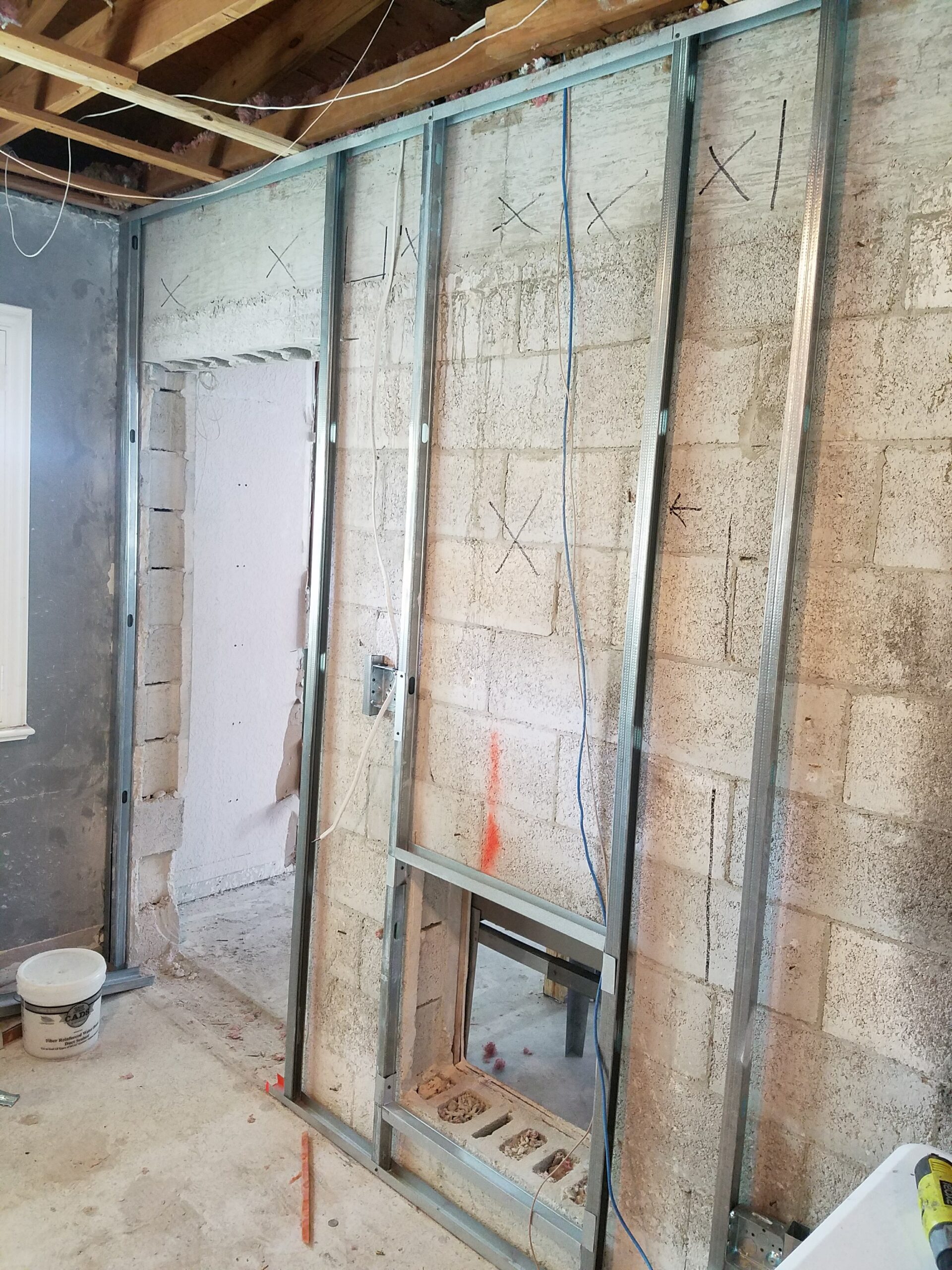 Interior renovation showing newly installed light-gauge metal stud wall framing with electrical rough-ins erected against an exposed concrete block wall